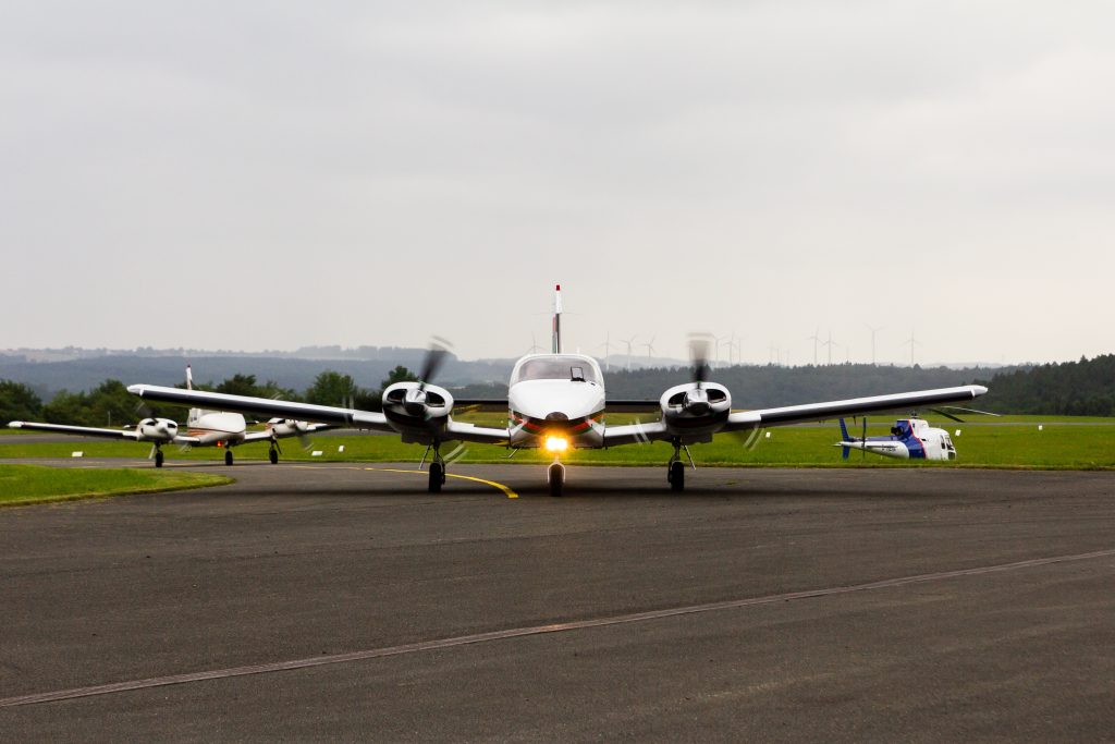 Two twin engine aircraft Piper PA 34 Seneca taxiing at Holzminden-Höxter airport with a wind farm on the background.